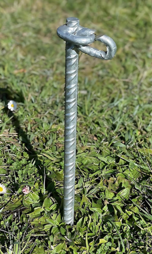 Piqueta (en uso) de hierro galvanizado en caliente, de 405 mm de largo y 20 mm de diámetro, con argolla soldada para sujeción. Ideal para anclar elementos en terrenos blandos. Se vende en paquetes de 10 unidades.